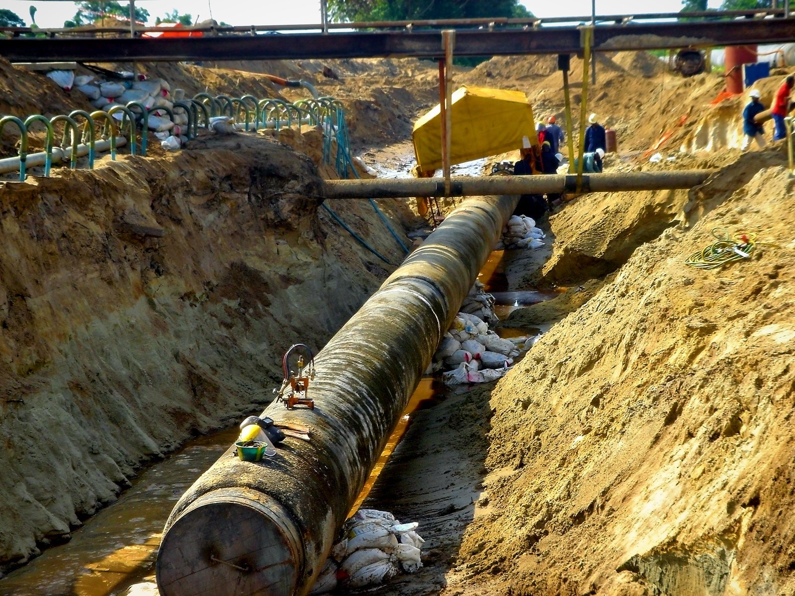 Pipe crossing tie-in in a dewatered trench beneath a temporary bridge