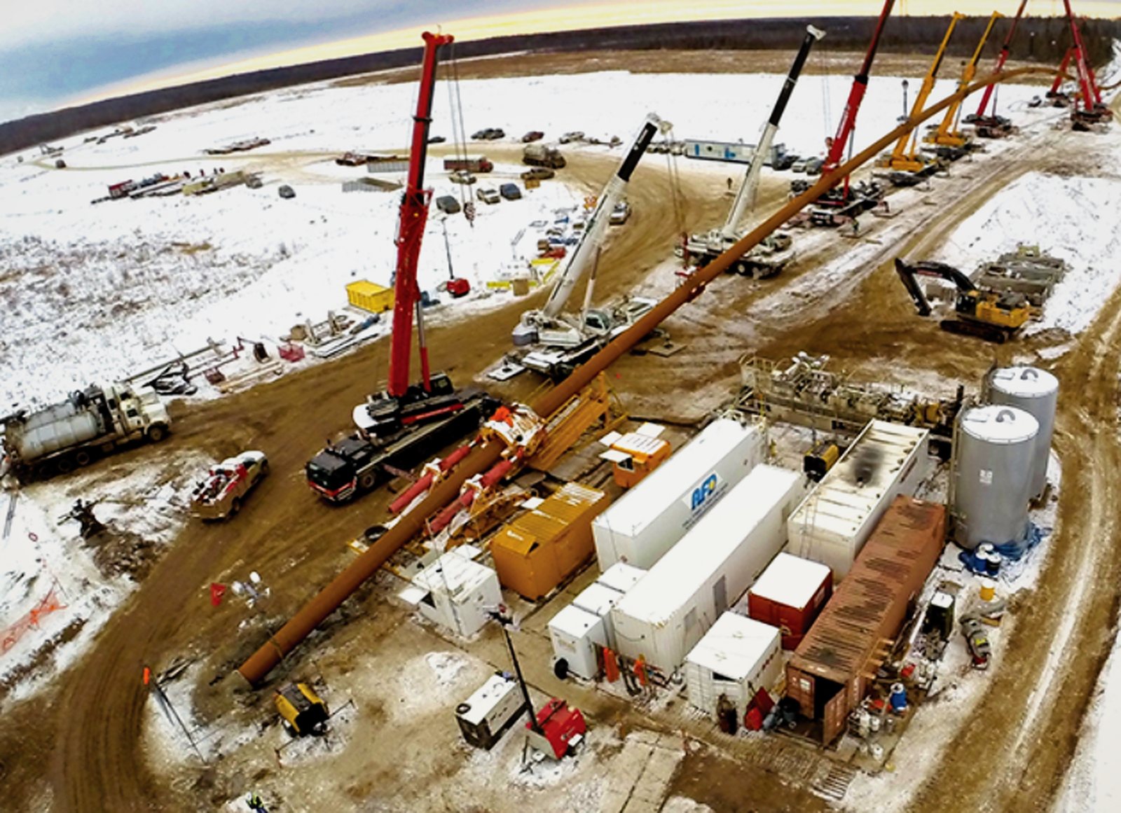 Aerial view of a large-diameter HDD site: drill rig, pipe string on rollers and support cranes