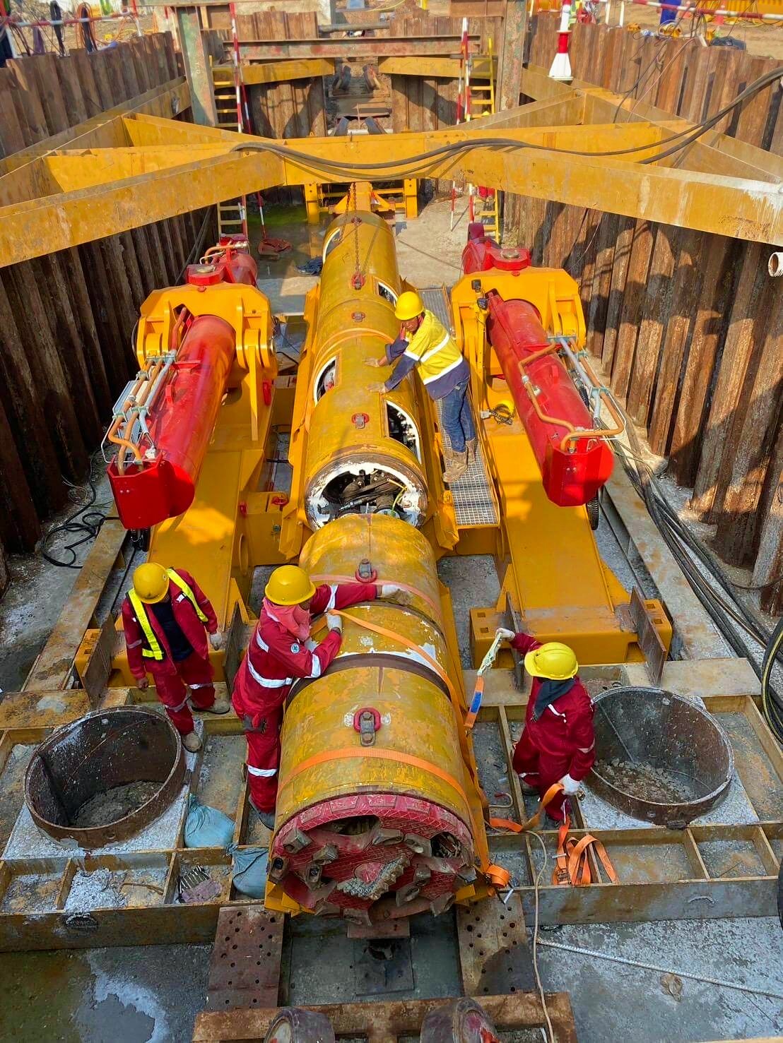 Microtunnel boring machine on the jacking frame in a sheet-piled launch shaft, with crew preparing the launch