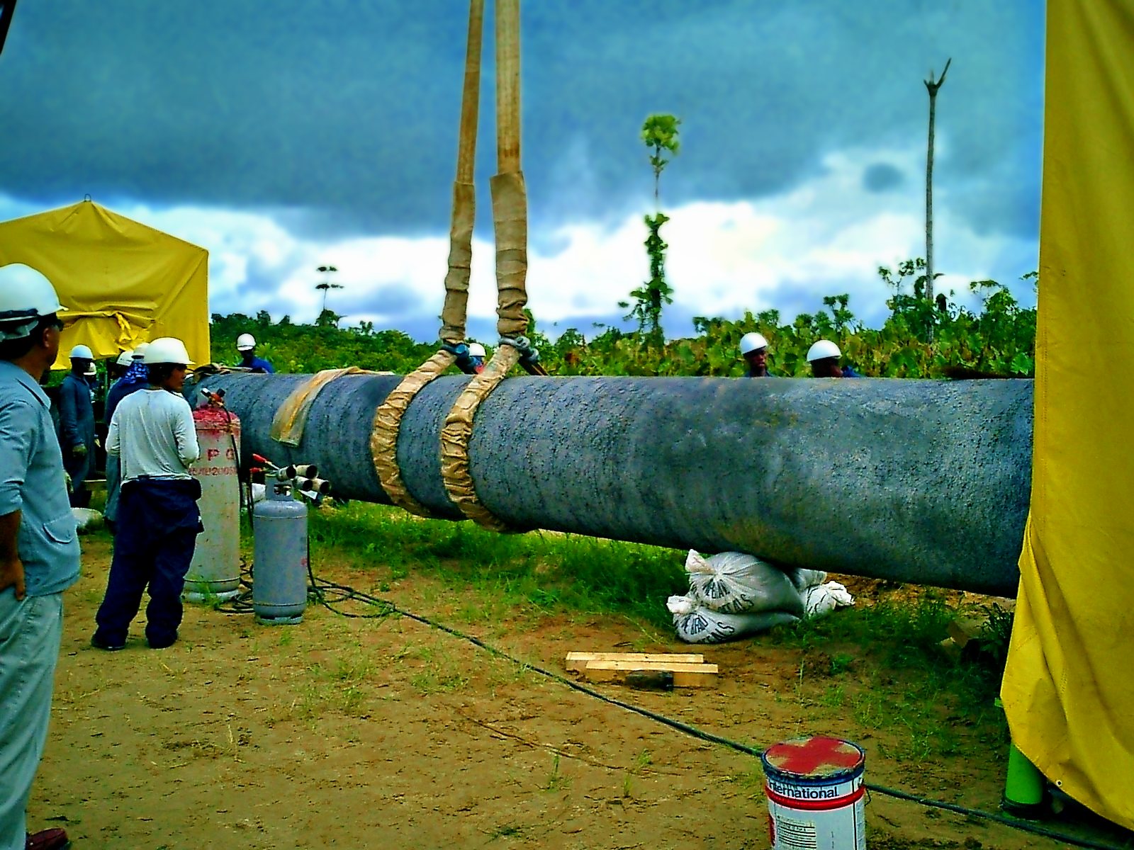 Supervised lift: crew in hard hats guiding a slung pipe joint into the weld shack