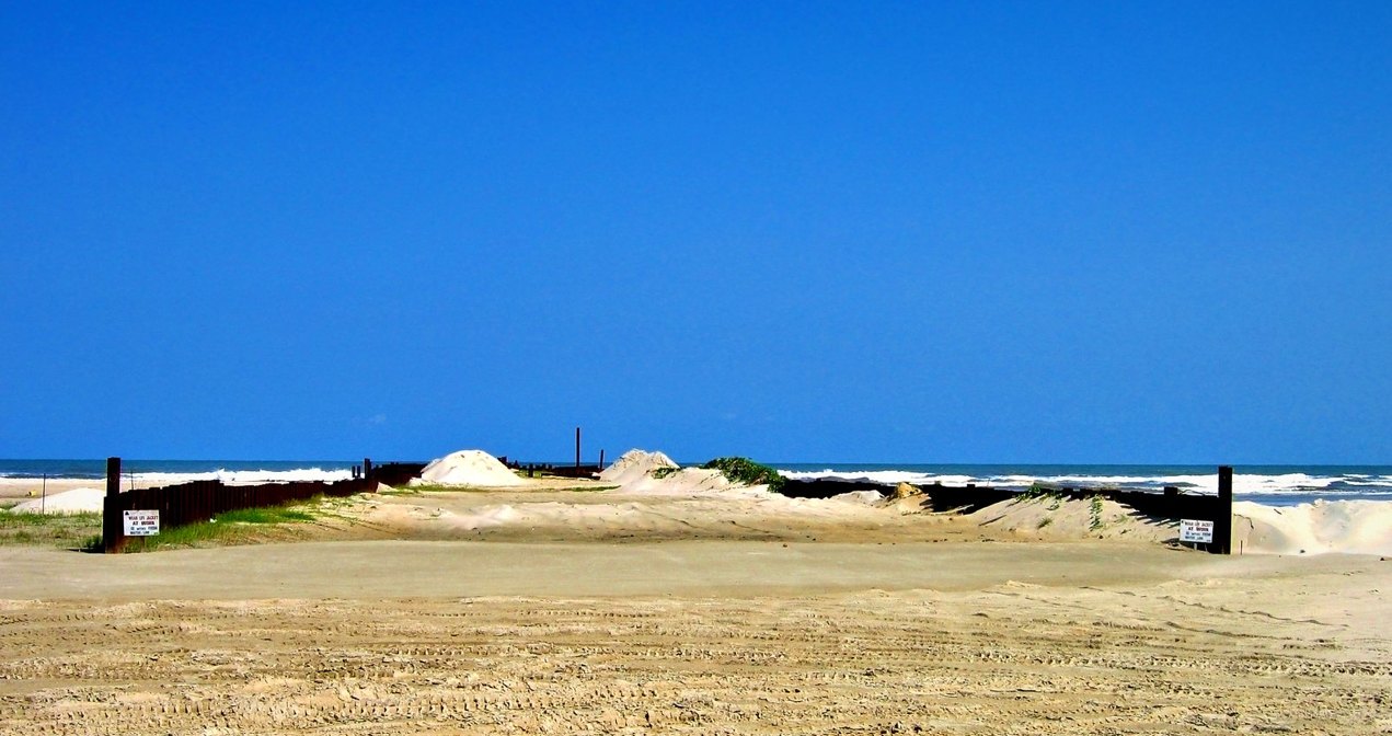 Completed sheet-pile cofferdam walls running across the beach to the surf