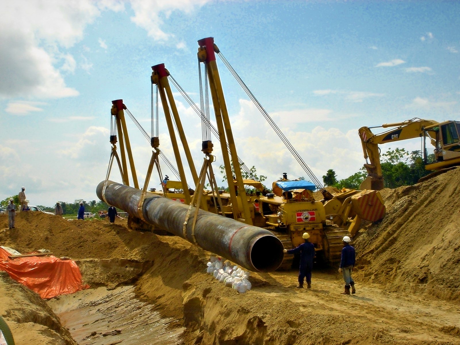 Sideboom tractors lowering a pipe section into the trench