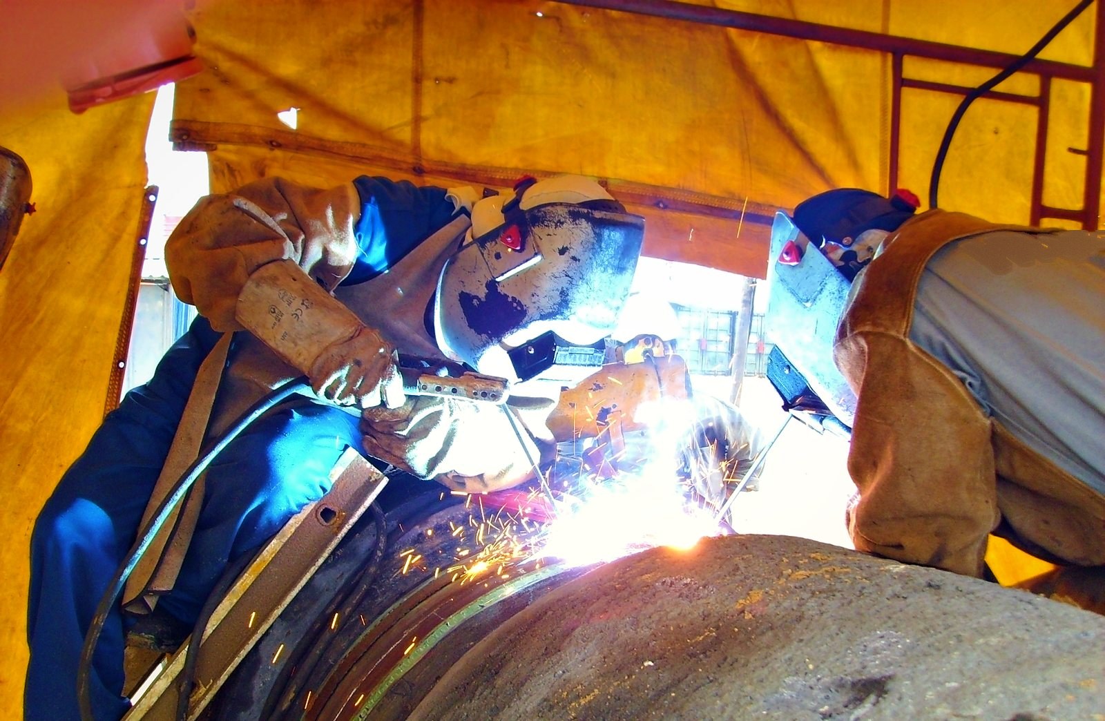 Two welders on a pipeline joint inside a welding shelter