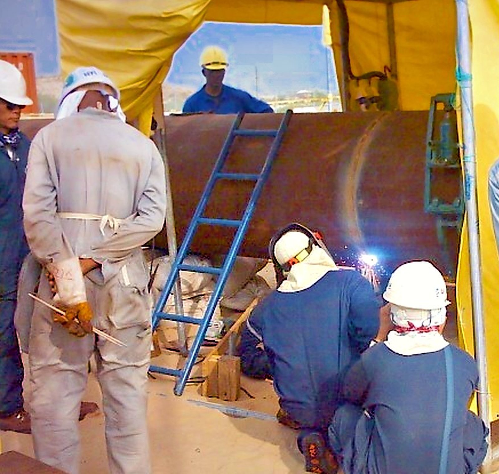 Welder qualification test in progress inside a welding tent, watched by inspectors